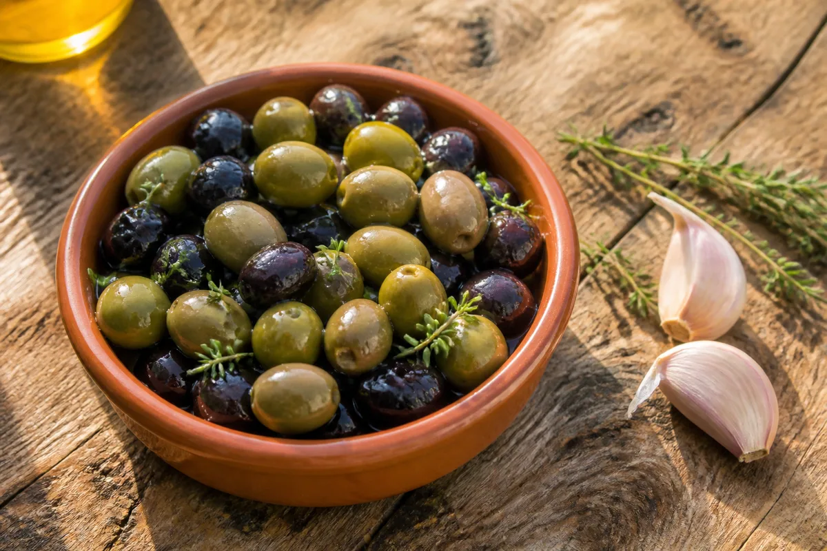 Coupelle de céramique unie garnie d’olives et de brins de thym sur une table en bois brut