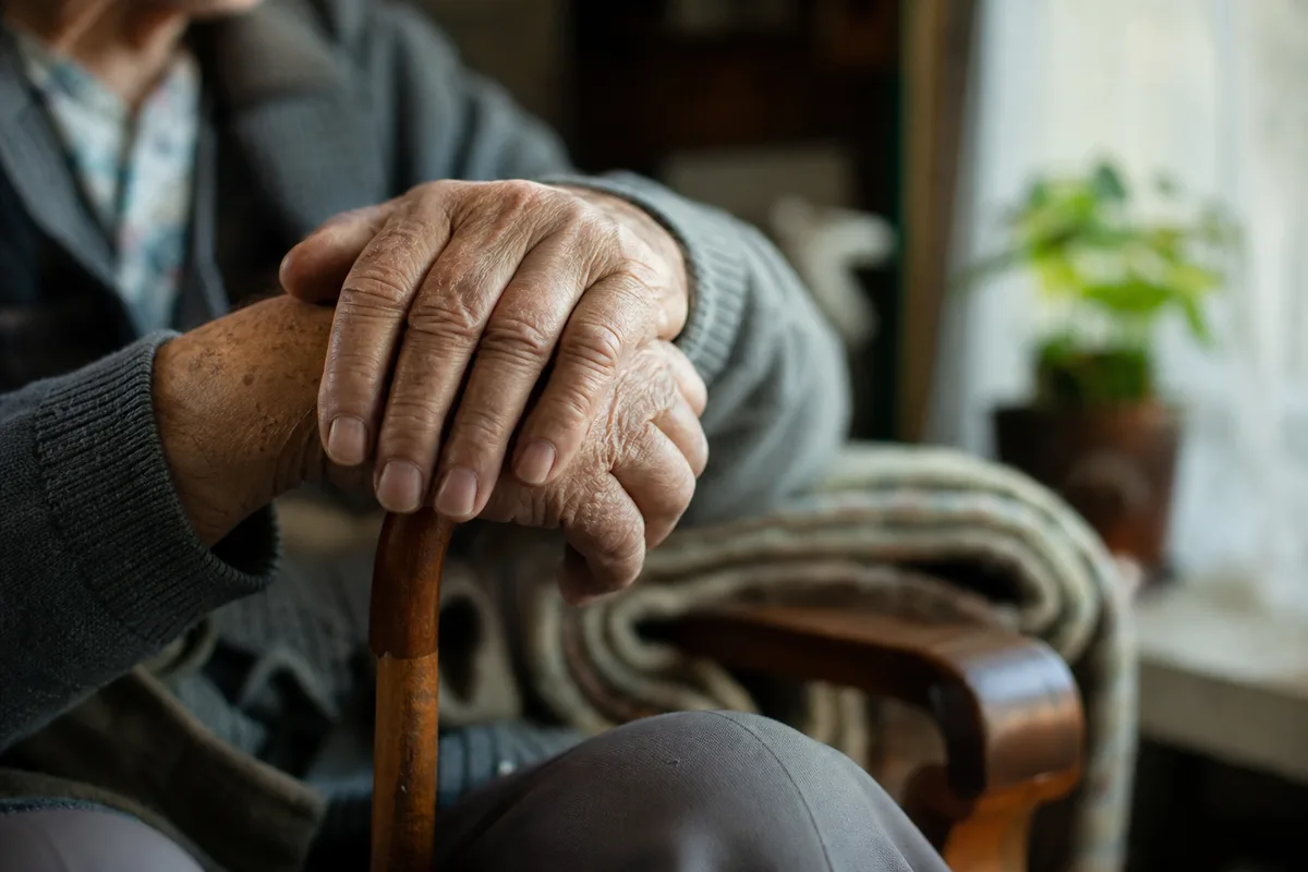 Mains d&rsquo;une personne âgée posées sur une canne, intérieur lumineux de domicile
